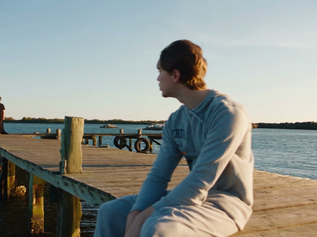 Original Raindance source frame with a man in a gray hoodie seated beside the water